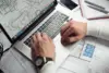 Architekt arbeitet am Laptop mit Bauplänen und Grundrissen für Immobilienprojekt auf dem Schreibtisch